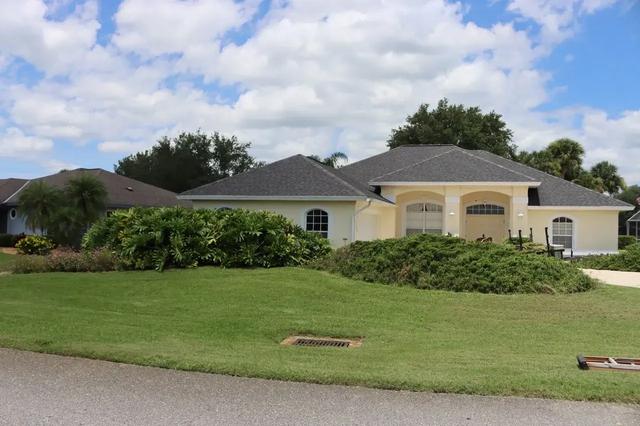 Single-story house with a manicured lawn, shrubs, and a cloudy sky