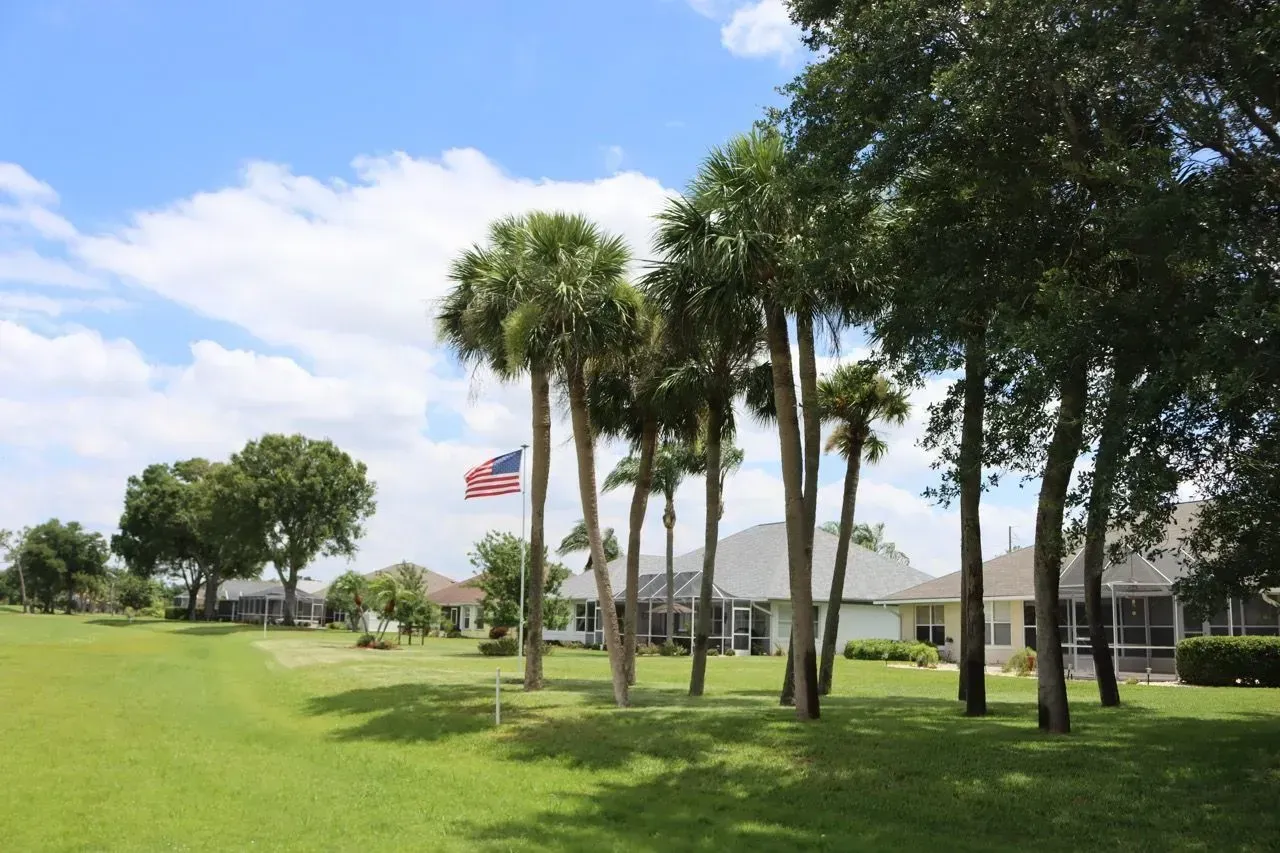 Palm trees and a U.S. flag on a grassy lawn beside a building under a blue sky.