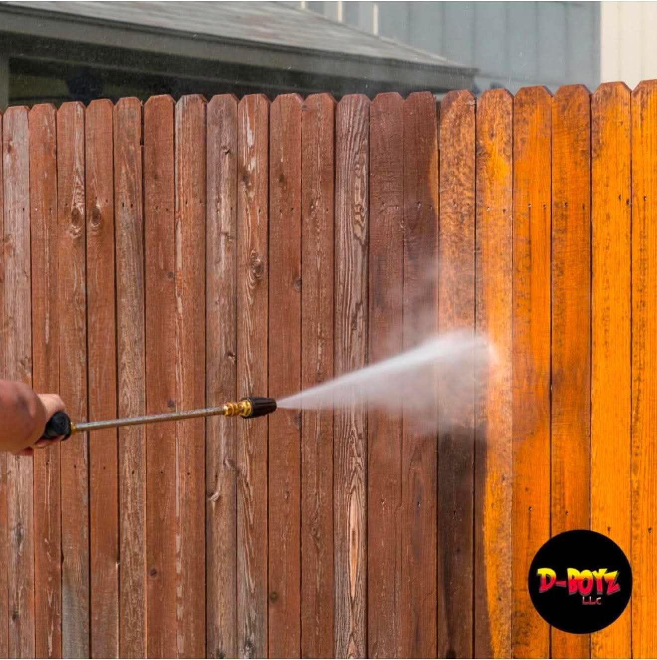 Person pressure-washing a wooden fence, with one section cleaned and bright orange compared to the rest.