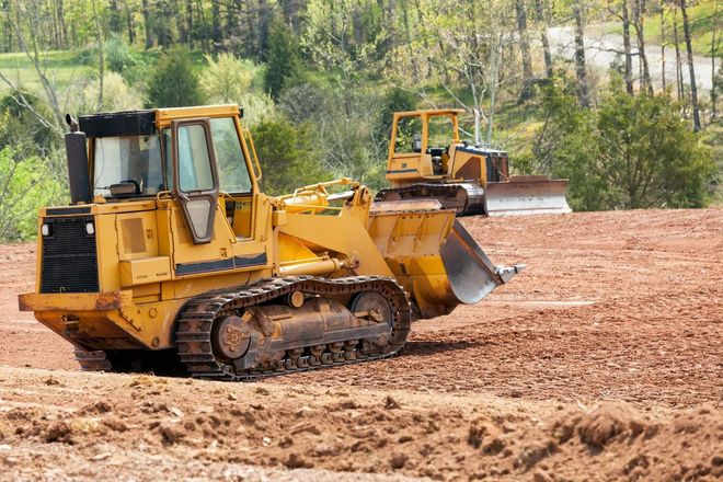 Yellow bulldozer pushing dirt on a muddy construction site, with another machine in the background.