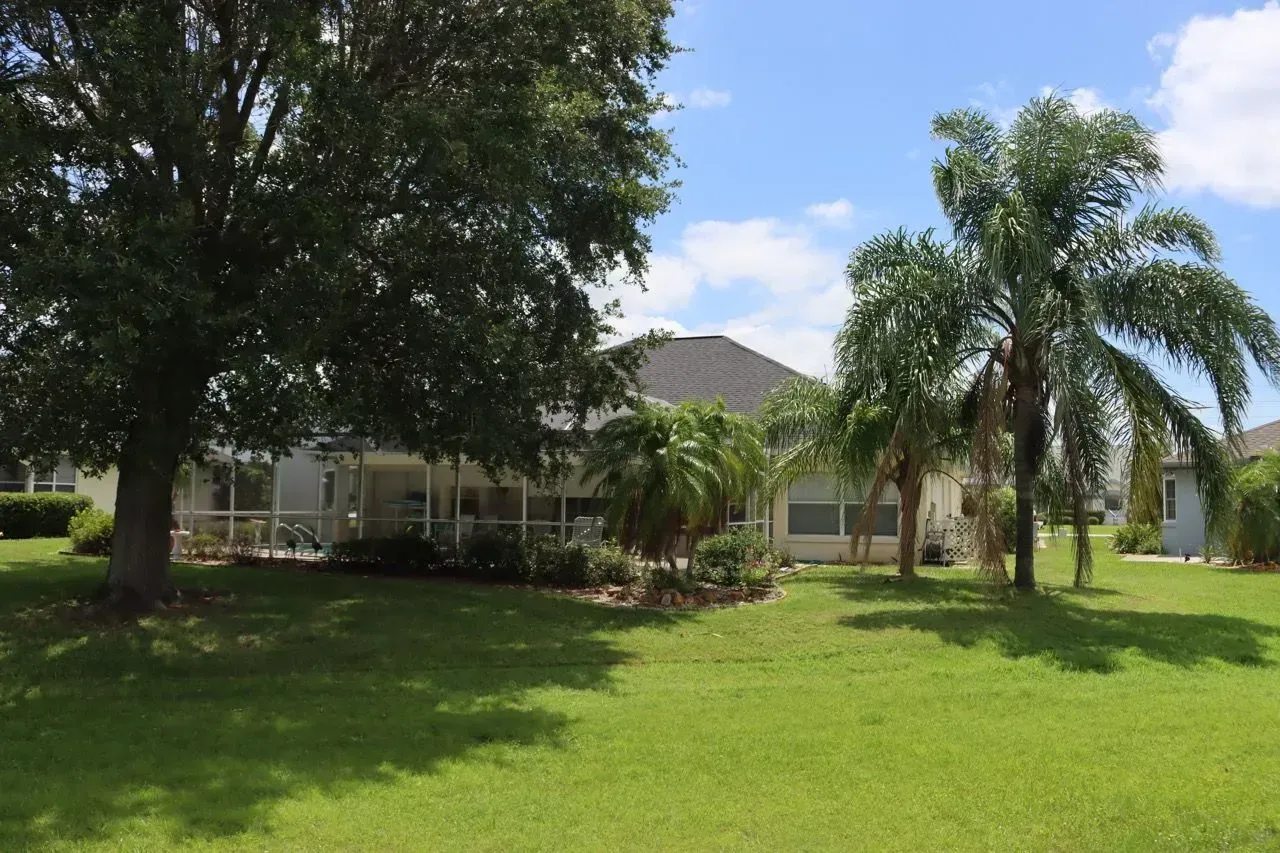 Suburban house with a large green lawn and palm trees under a partly cloudy sky