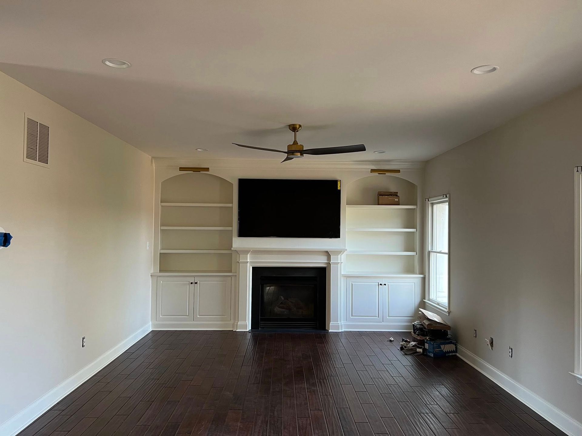 Living room with dark wood floors, a fireplace, built-in white bookshelves, a black TV, and a ceiling fan.