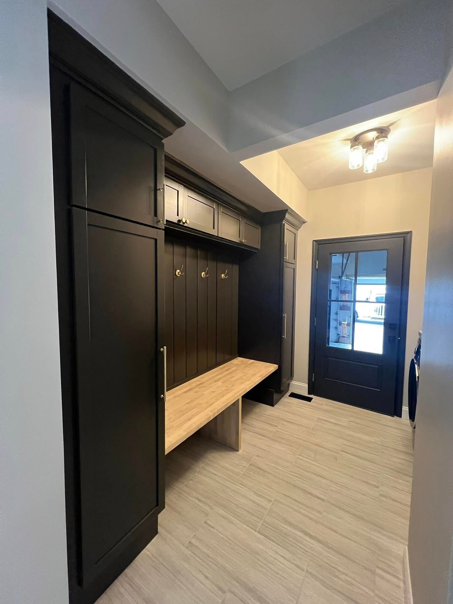 A dark, built-in entryway unit with a bench, coat hooks, and storage cabinets; a front door is visible.