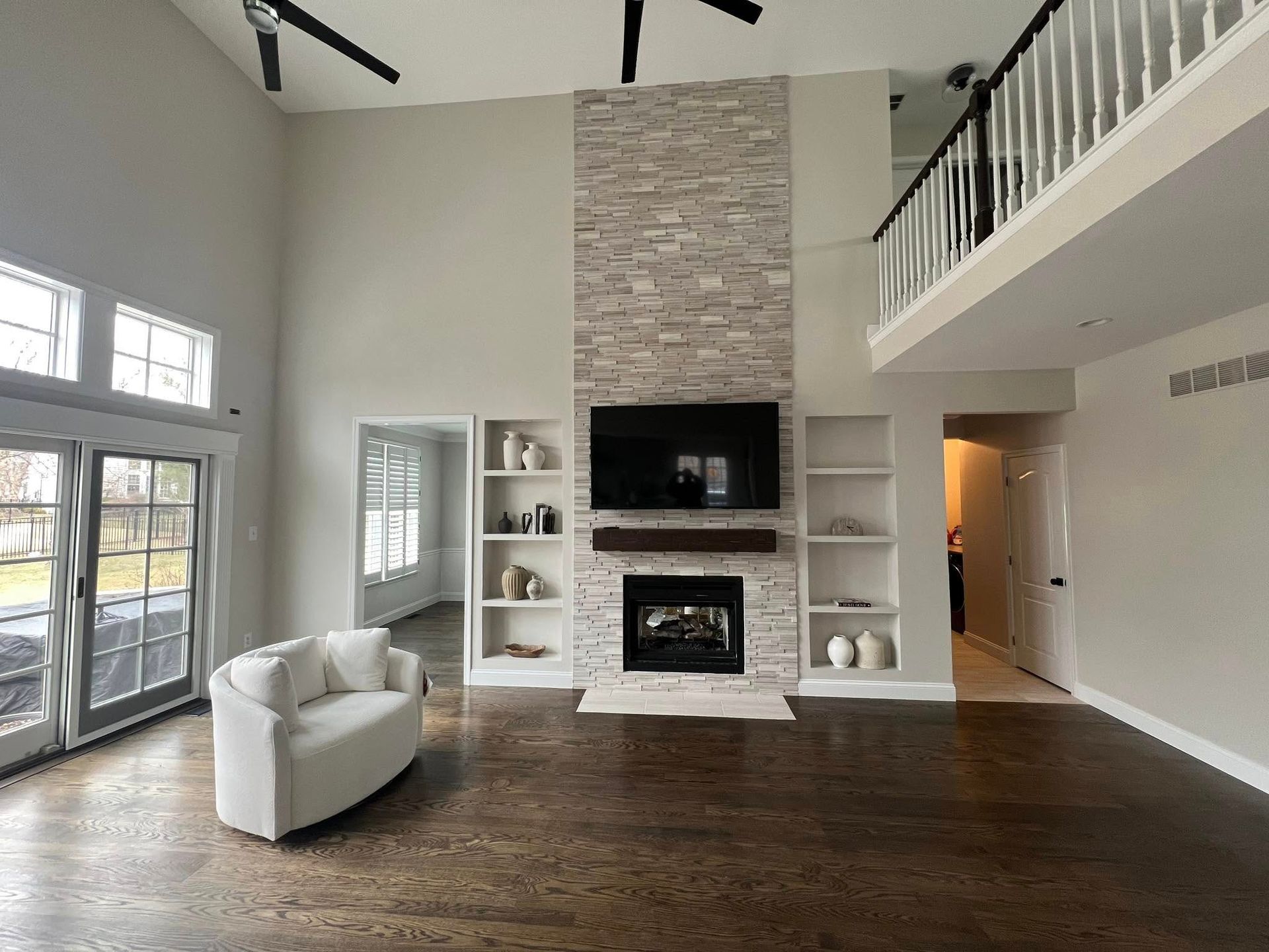 Spacious living room with a fireplace, built-in shelves, and a loft. Dark hardwood floors contrast with light walls and a white sofa.