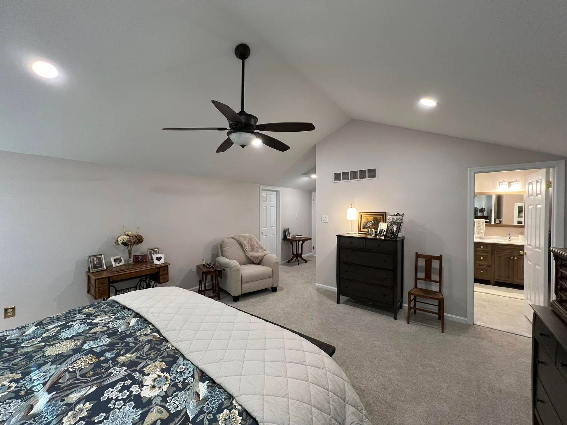 A bedroom with a bed, chair, dresser and ceiling fan.