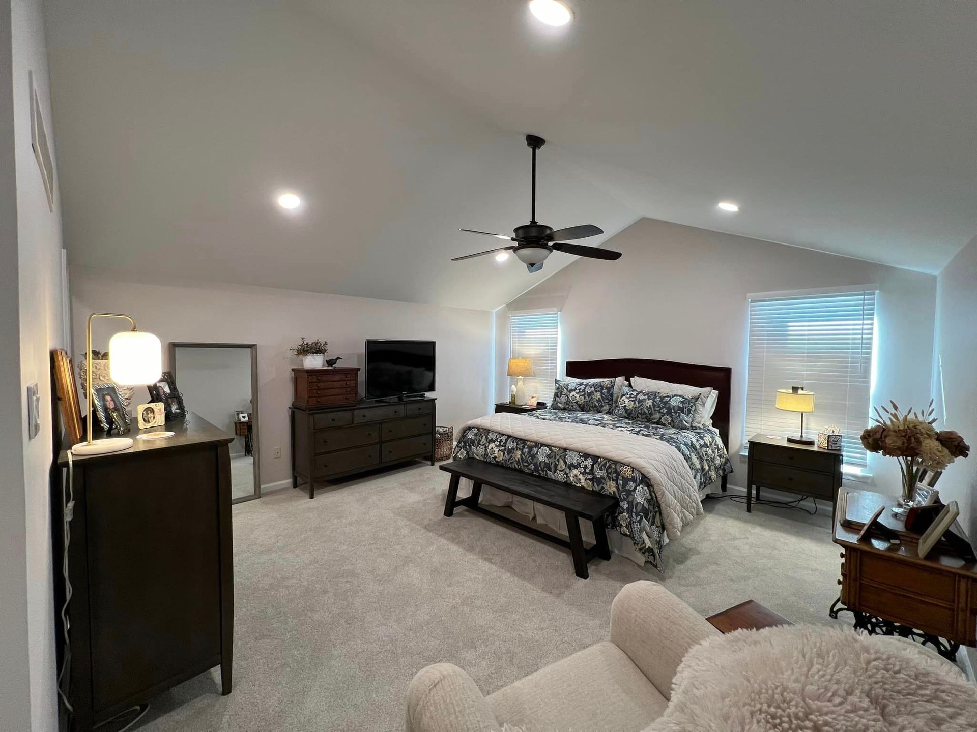 A bedroom with a bed, dresser, chair and ceiling fan.