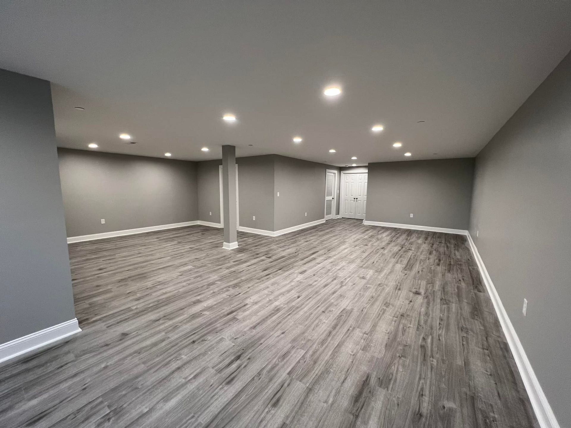 An empty basement with a wooden floor and gray walls.