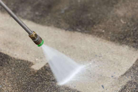 Pressure washer spraying water onto a concrete surface, cleaning a visible section.