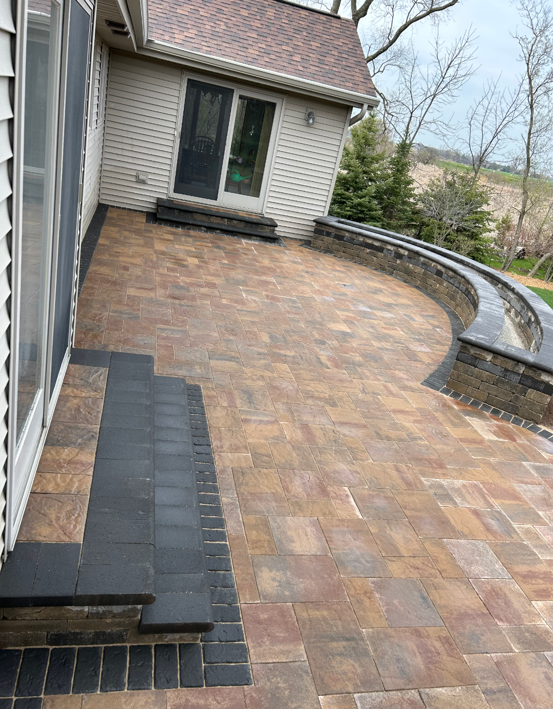 Brick patio with curved retaining wall and house in the background.