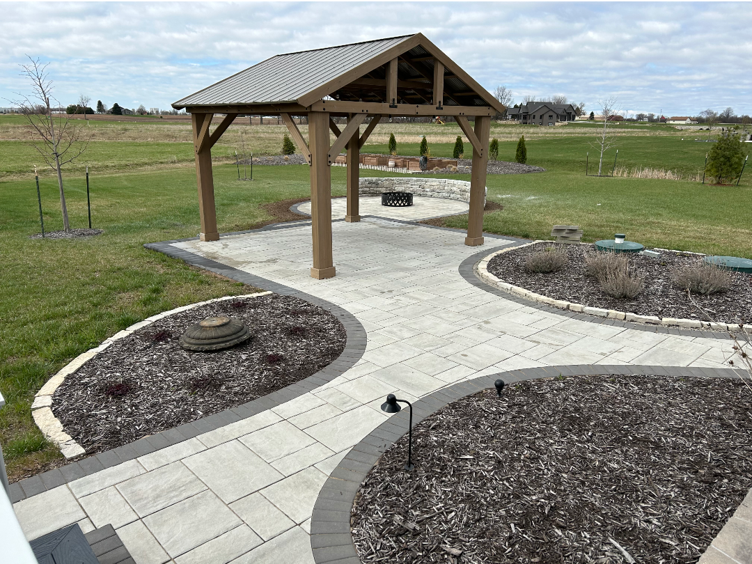 Gazebo with a stone patio, surrounded by landscaped areas on a green lawn.