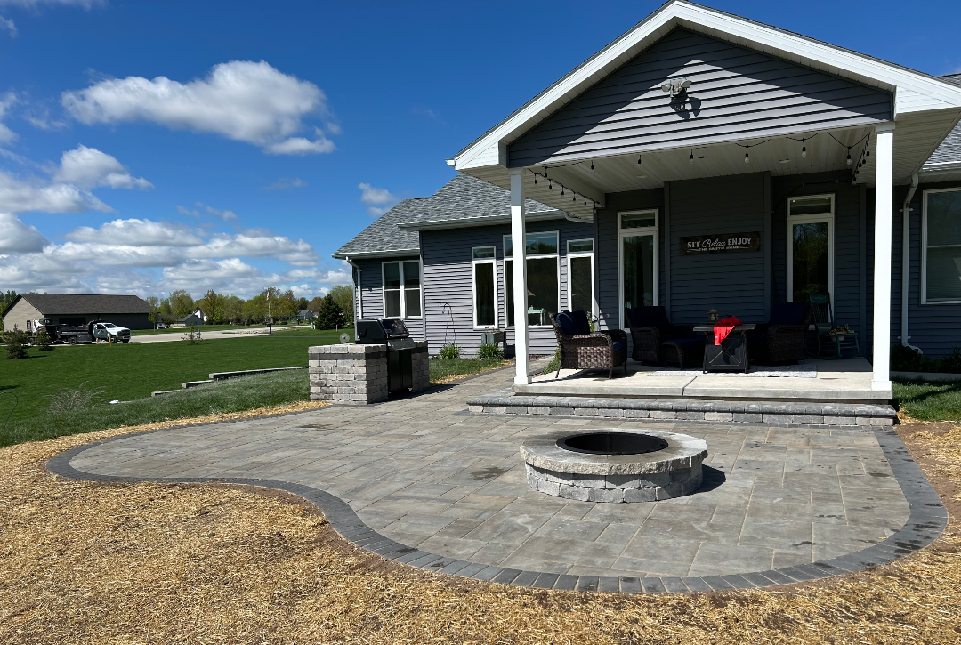 Backyard patio with fire pit, grill, and covered porch on a sunny day.