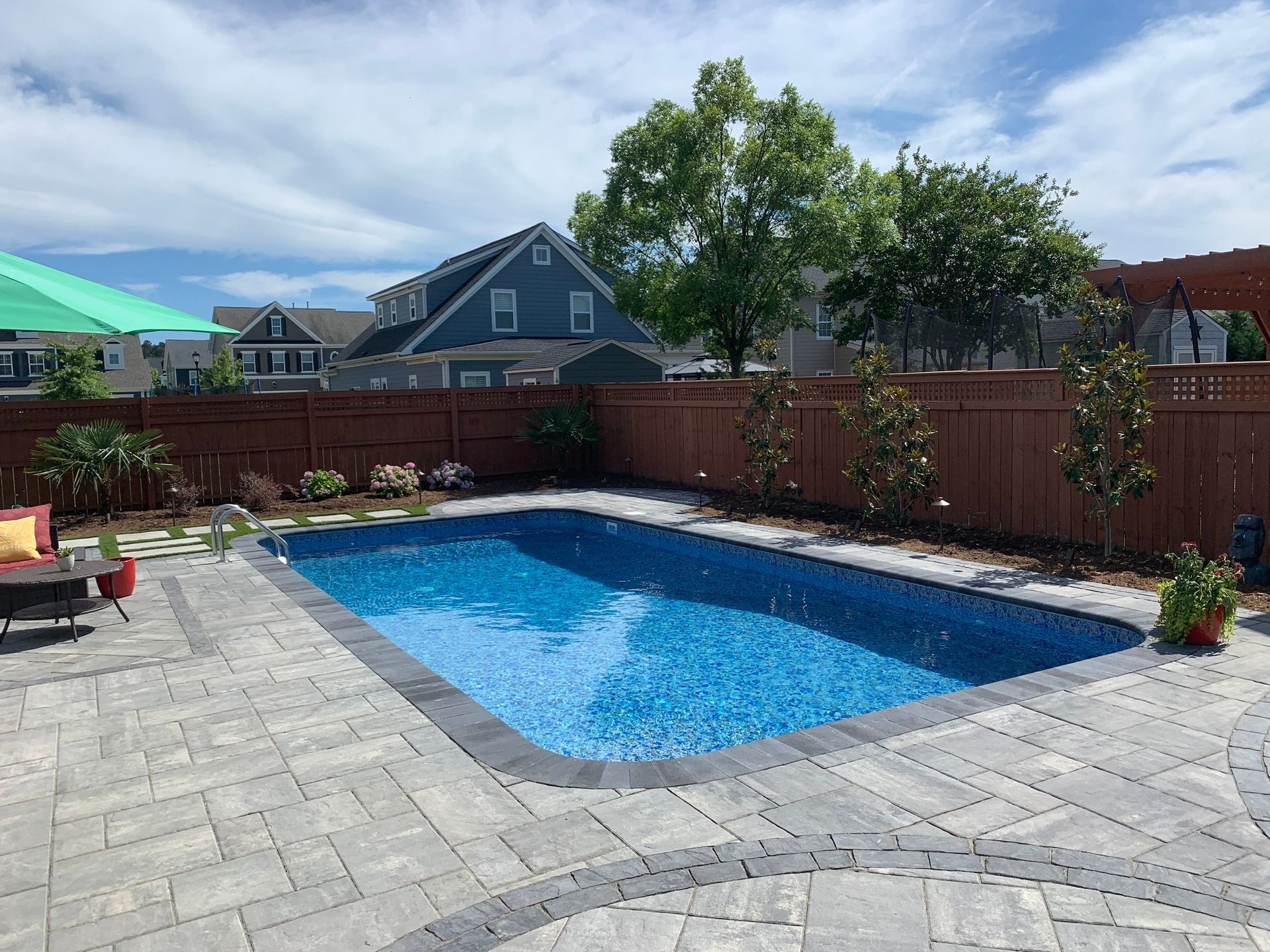 a large swimming pool is surrounded by a brick patio and a wooden fence