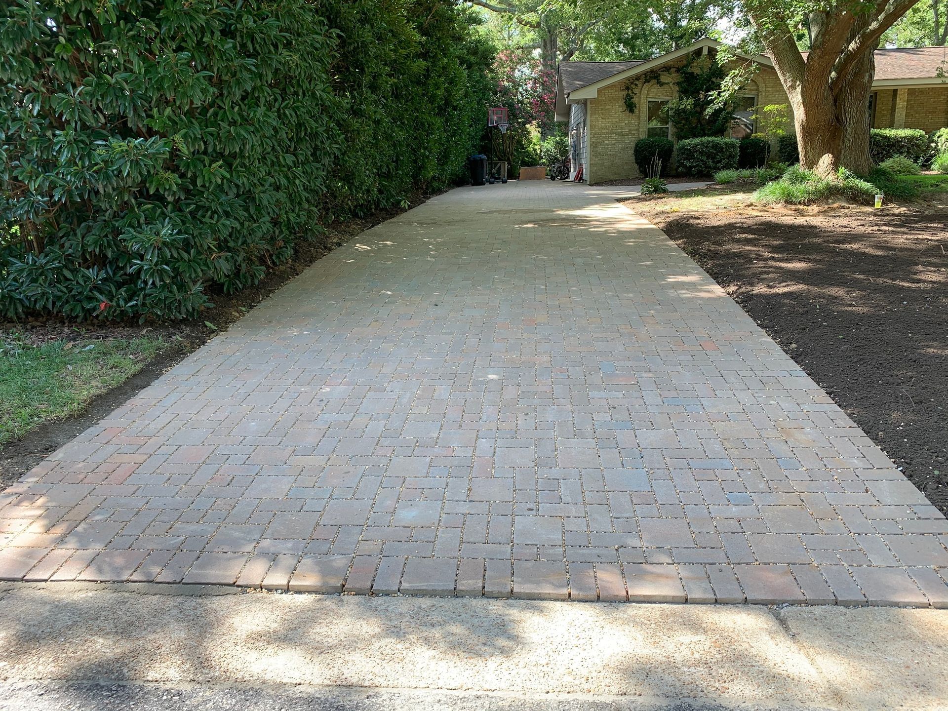 a brick driveway leading to a house surrounded by trees