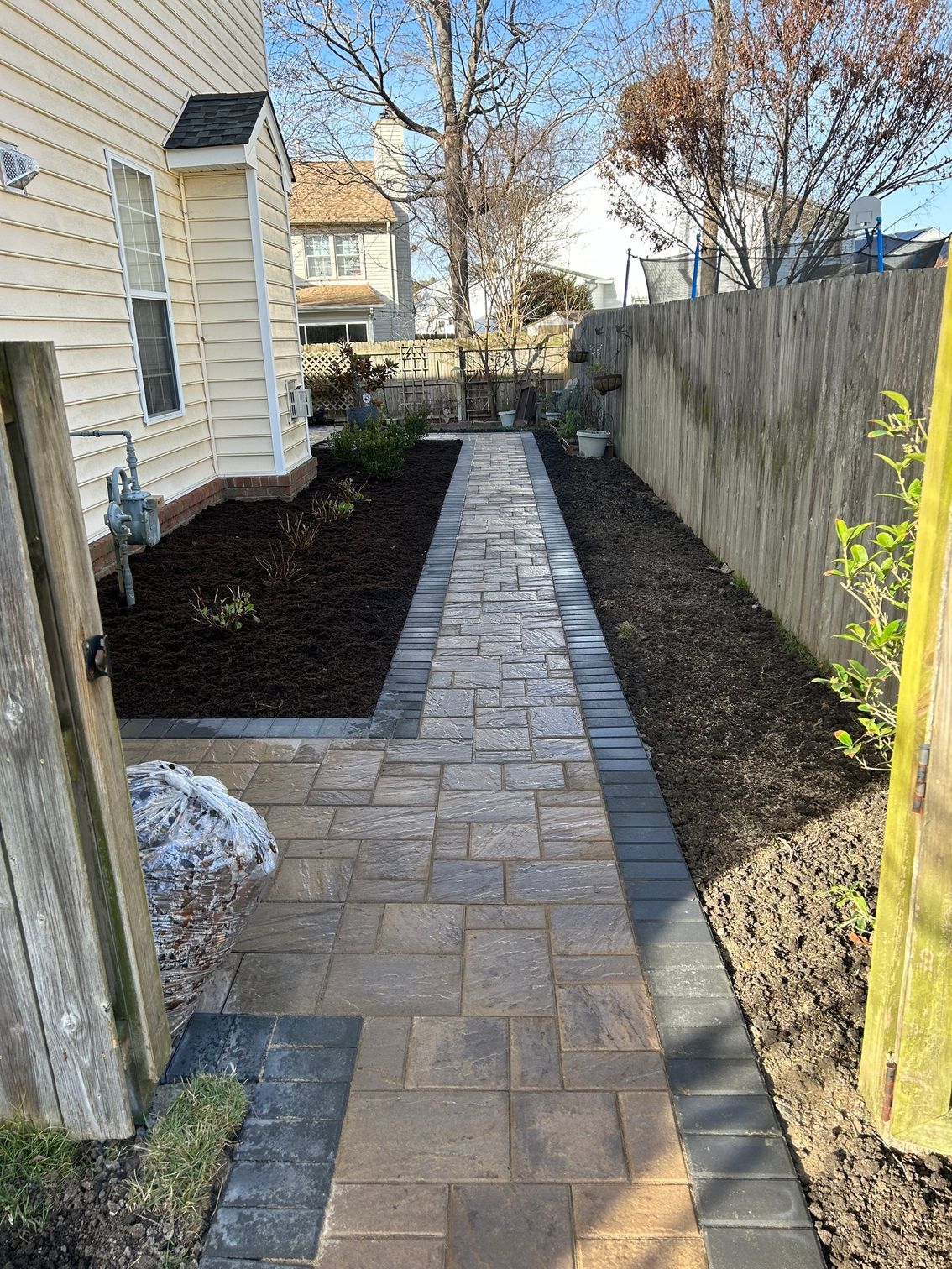 a brick walkway leading to a house next to a fence