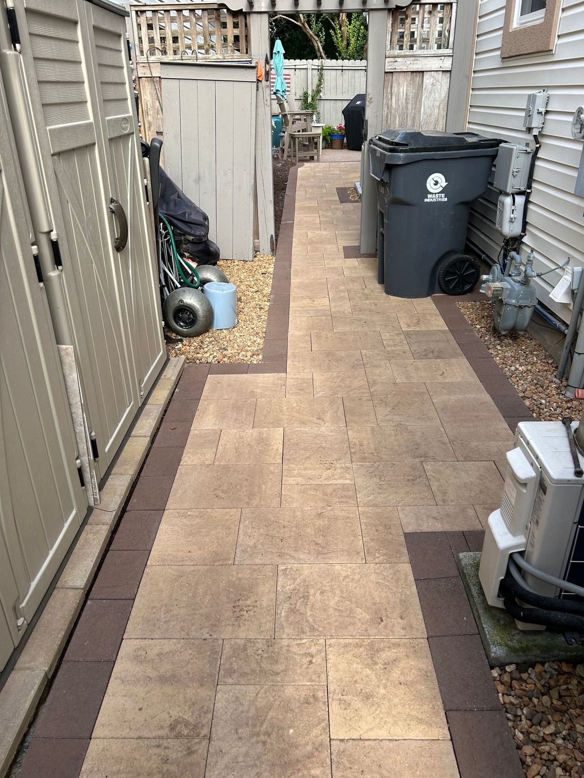 a brick walkway leading to a trash can in a backyard