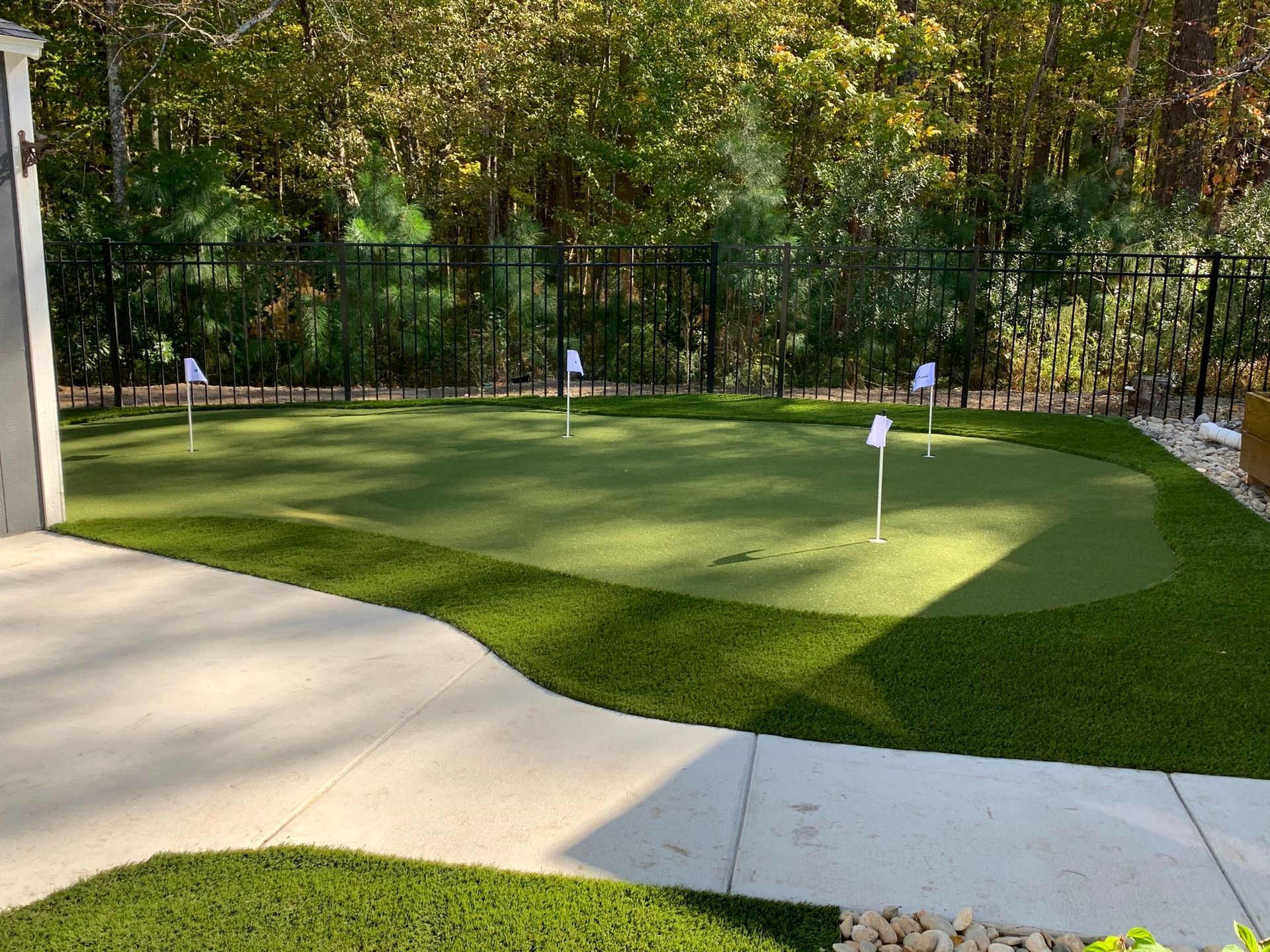 a backyard putting green with a fence and trees in the background
