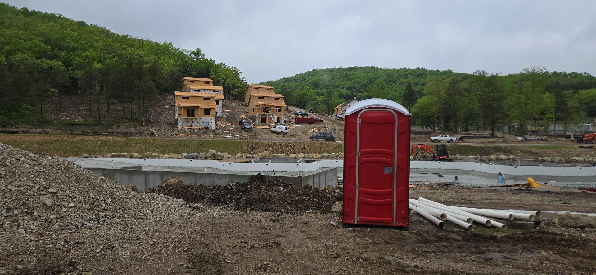 A red portable toilet is sitting in the middle of a construction site.