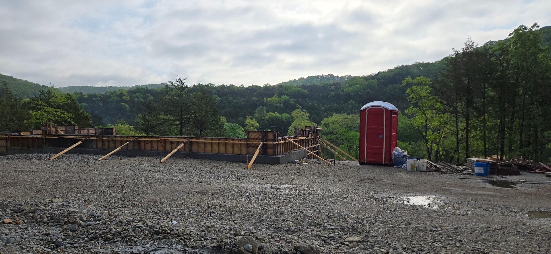 A red portable toilet is sitting in the middle of a gravel field.