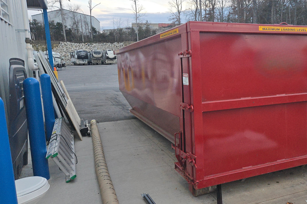 A large red dumpster is sitting in a parking lot next to a toilet
