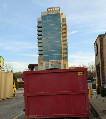 A red dumpster is parked in front of a Hilton hotel