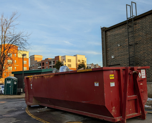 A large red dumpster is parked in front of a brick building