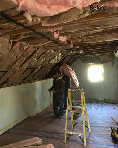 A man is standing on a ladder in an attic.