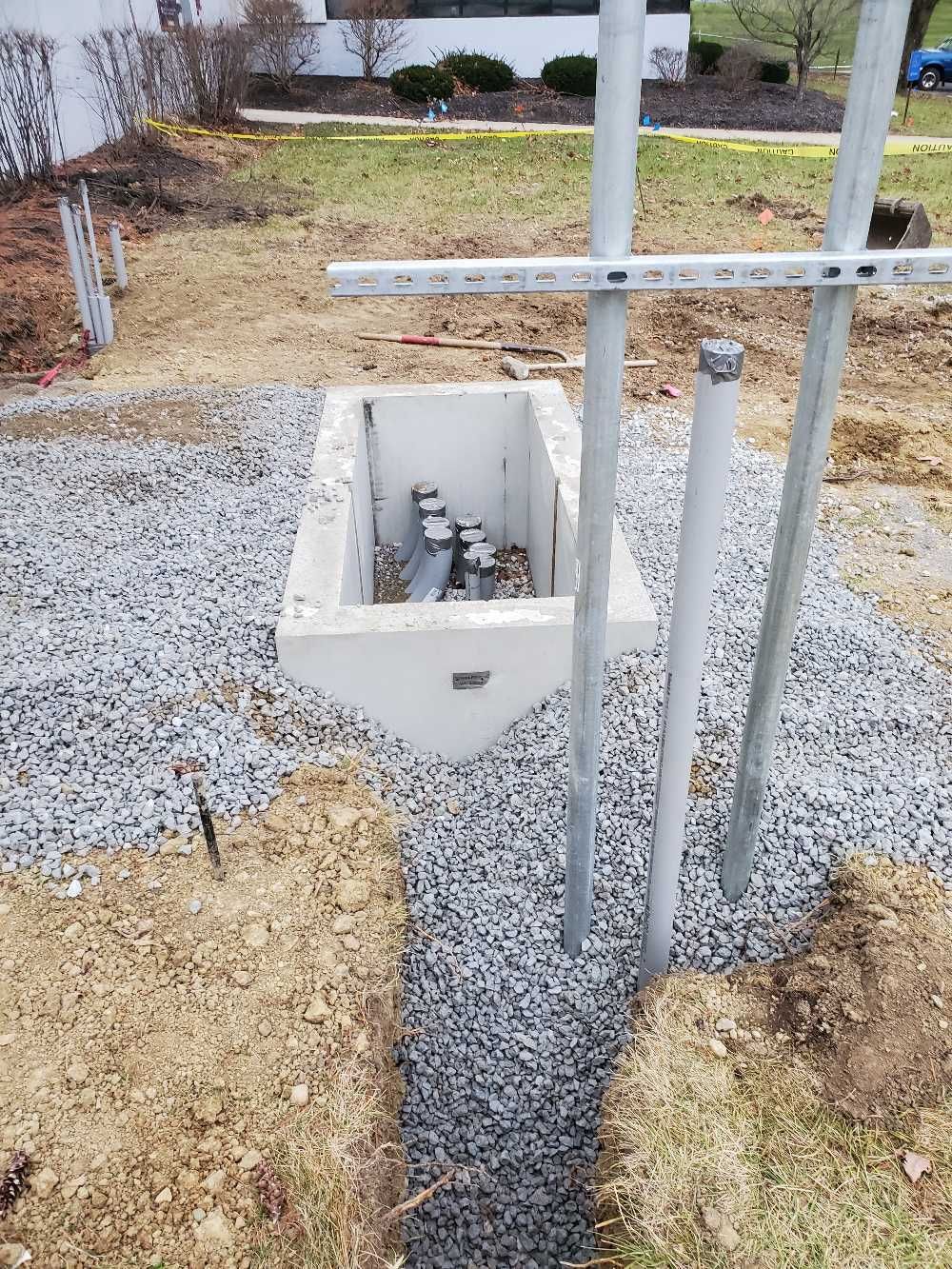 A concrete box is sitting in the middle of a gravel area next to a metal pole.