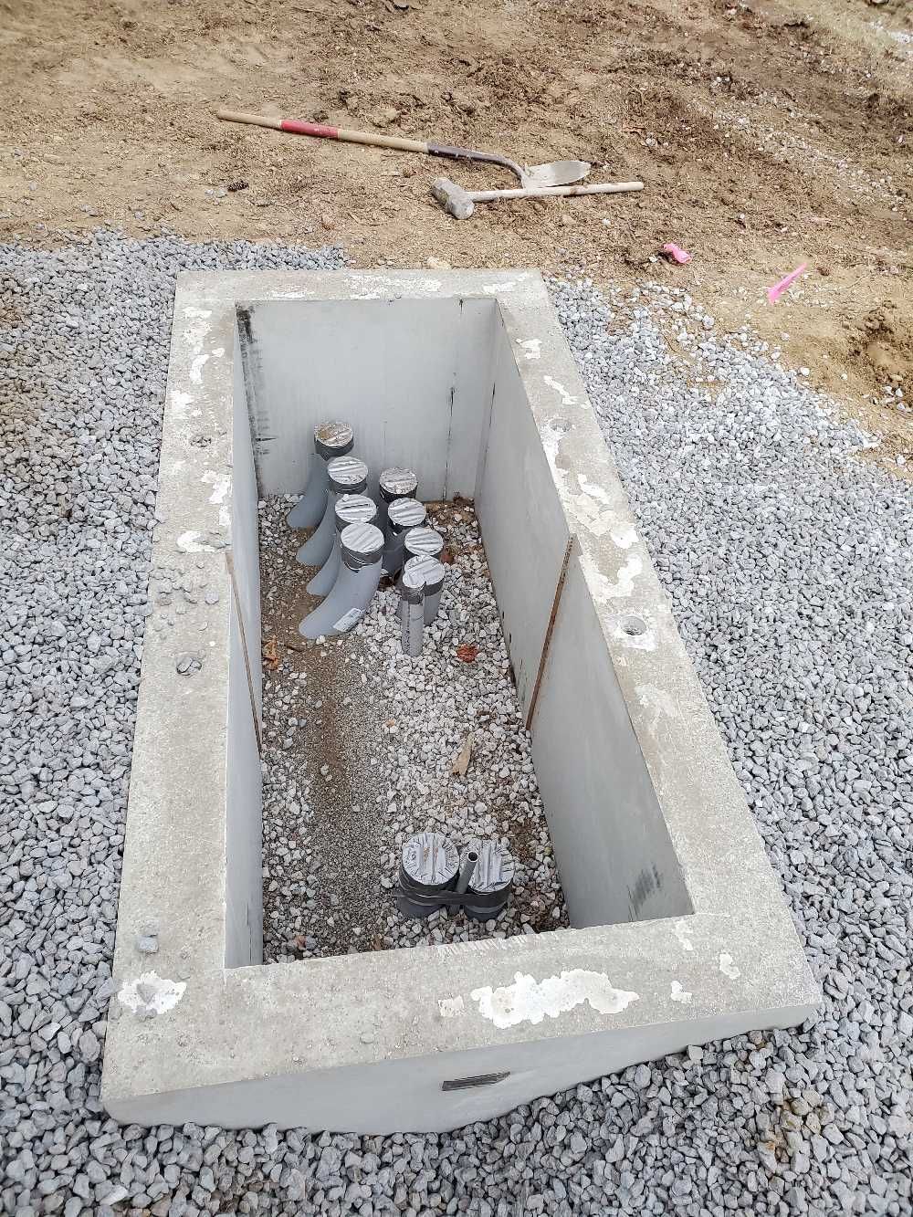 A concrete box with screws in it is sitting on gravel.