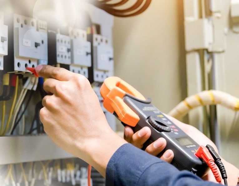 An electrician is using a clamp meter to test a circuit board.