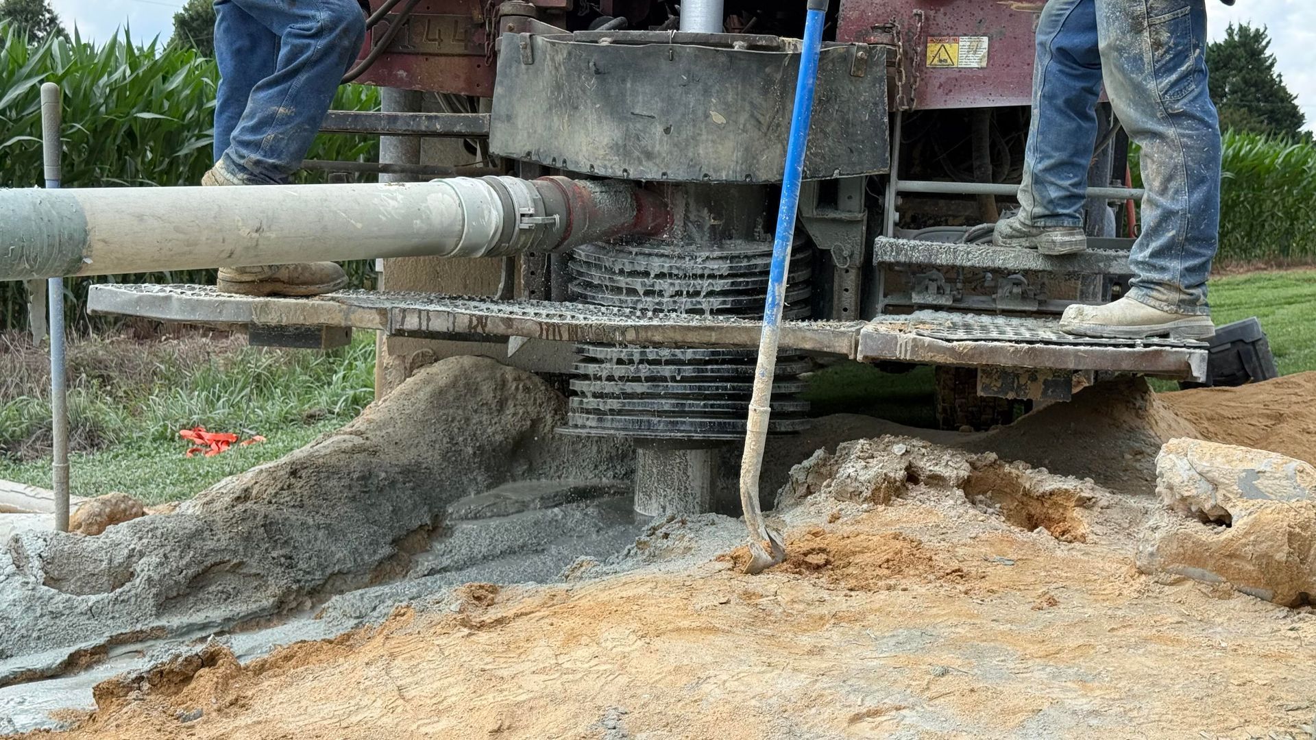 A man is standing next to a machine that is drilling a hole in the ground.