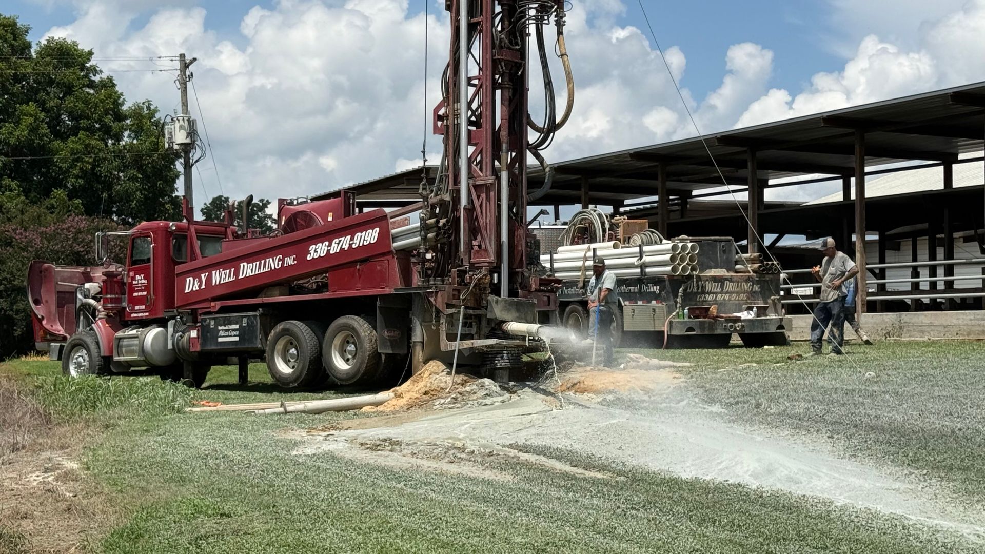 A red truck is drilling a hole in the ground in a field.
