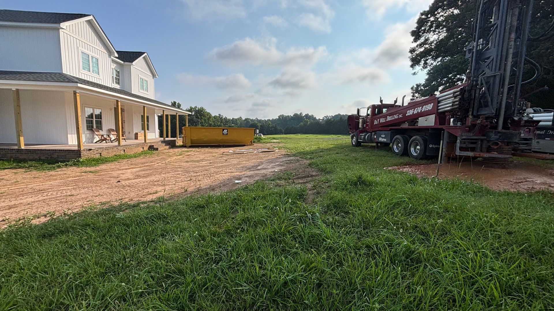 A red truck is parked in a grassy field in front of a house.