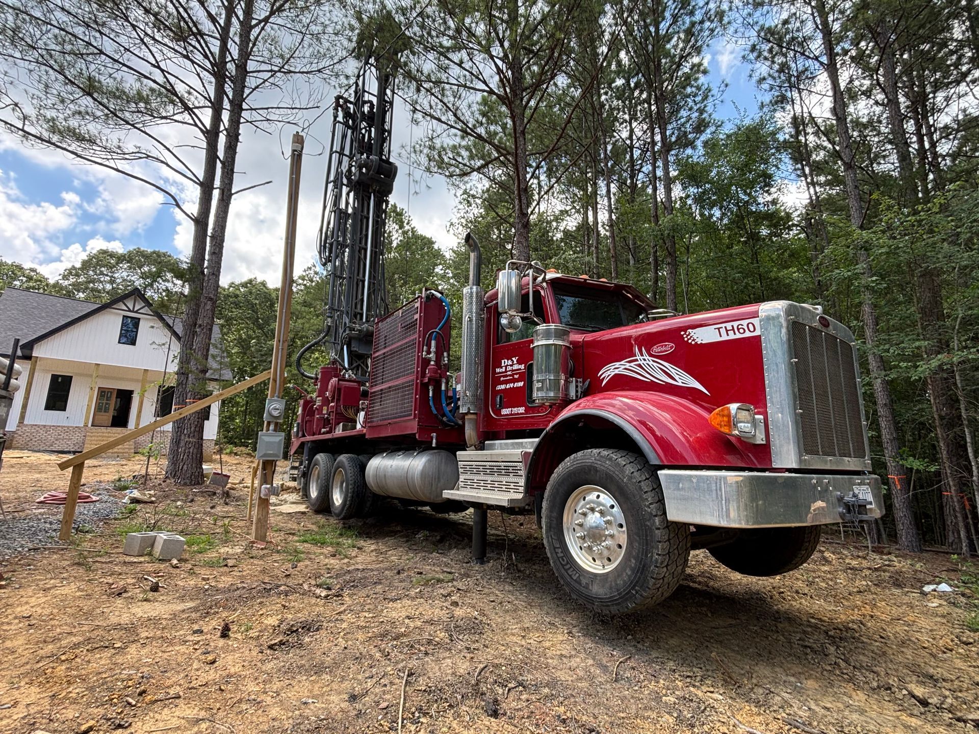 A red semi truck is parked in a dirt field in front of a house.