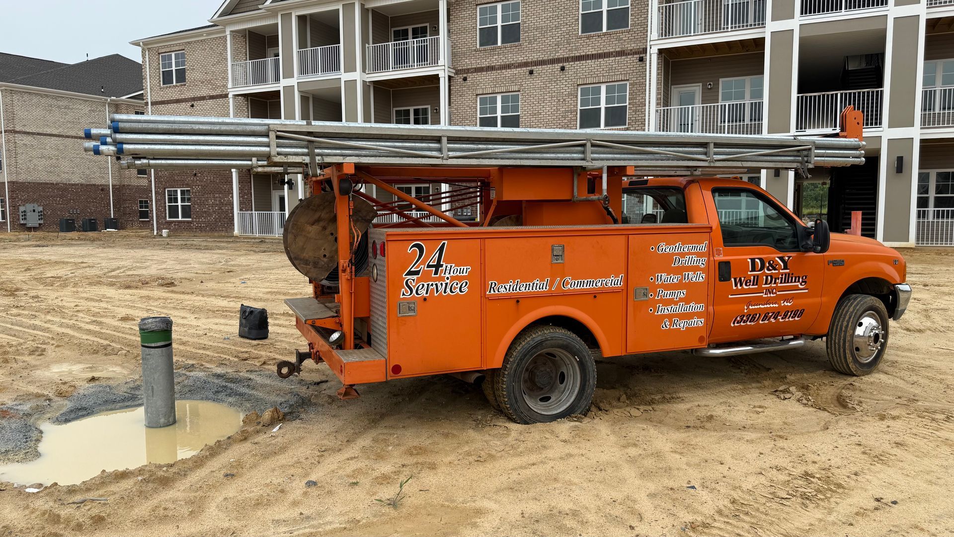 An orange truck is parked in a dirt field in front of a building.