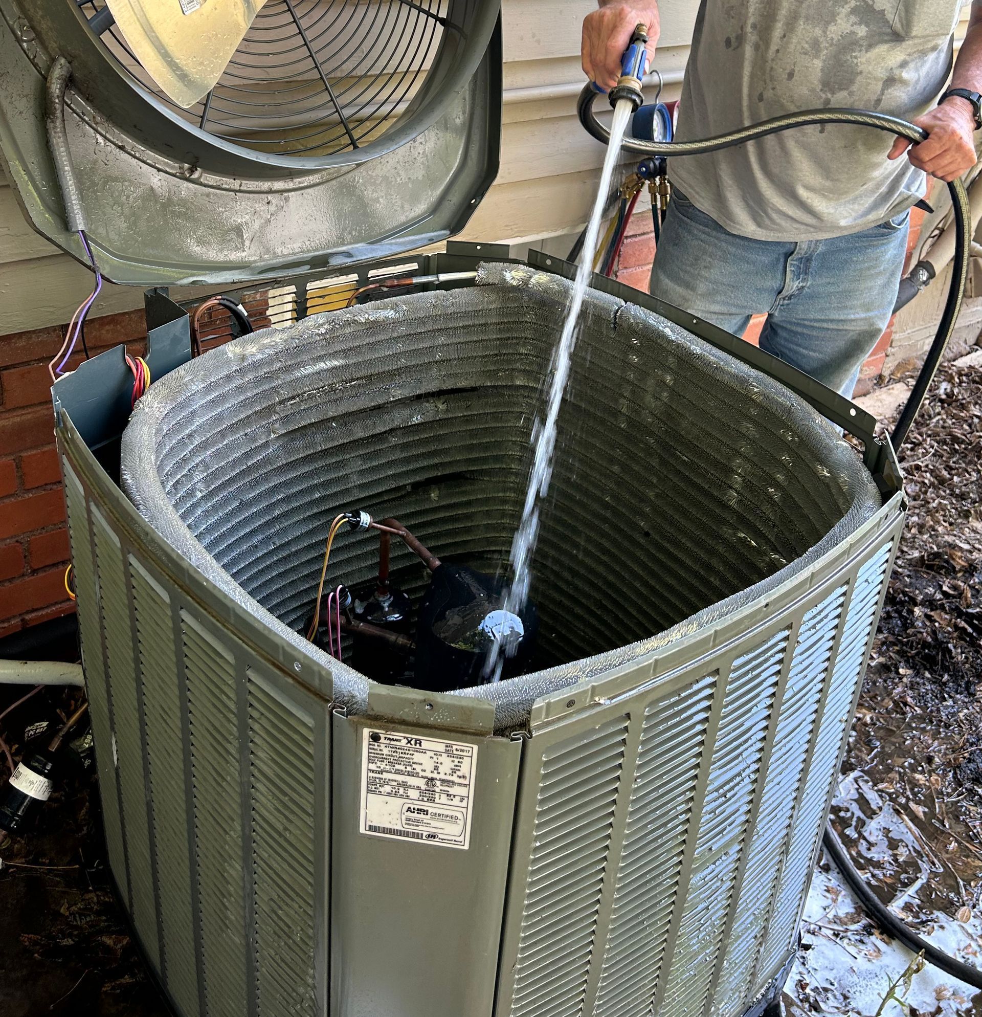 A man is cleaning an air conditioner with a hose.