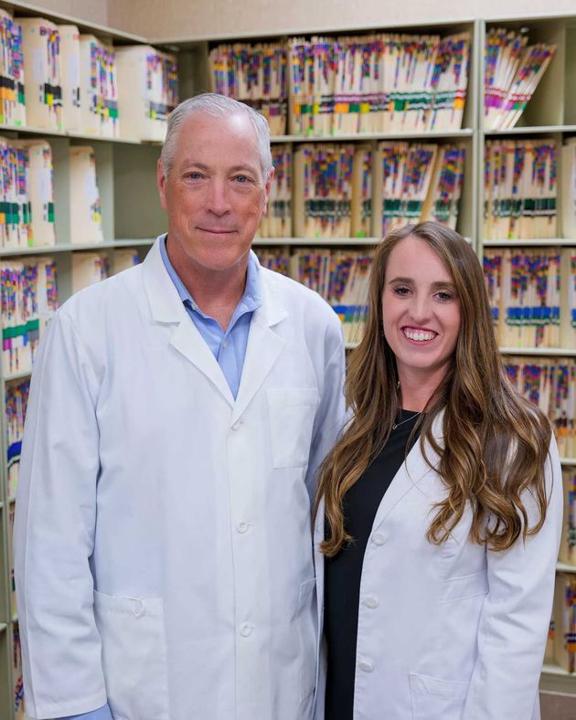 A professional in a white lab coat stands next to a colleague in a white lab coat in front of rows of medical files.