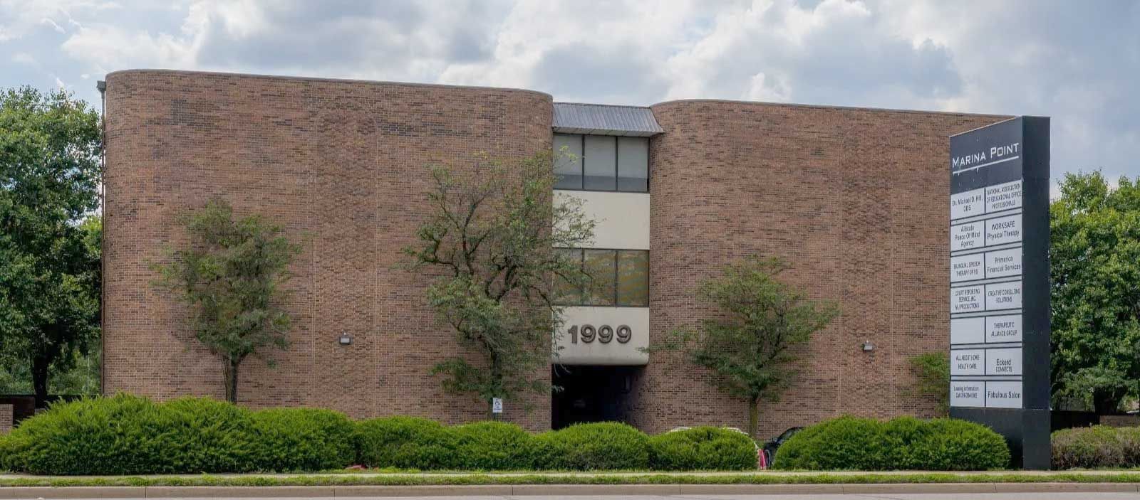 A three-story, brown brick office building with a central entrance marked "1999" and an adjacent tenant directory sign.