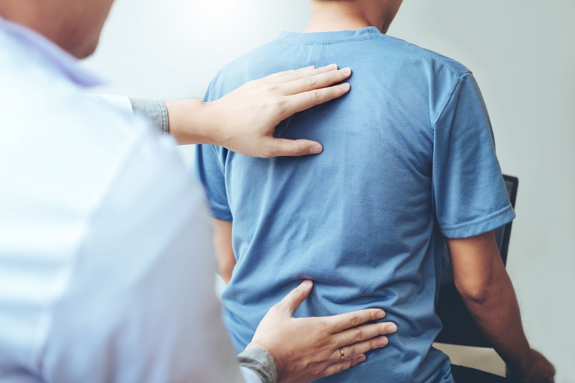 Person in blue shirt being examined on the back by a clinician in a white coat