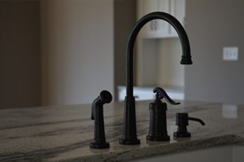 Black kitchen faucet, sprayer, and soap dispenser on a granite countertop.