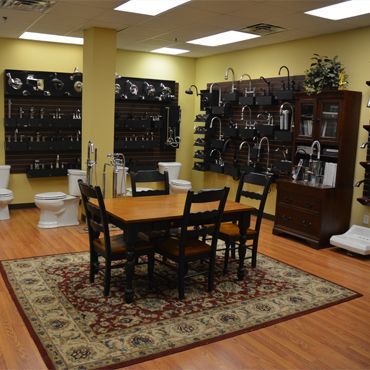 Bathroom fixtures showroom with a dining table and displays of faucets and toilets.