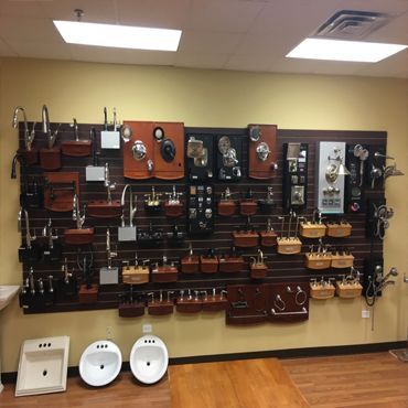 Bathroom fixtures displayed on a wall in a showroom, including faucets, handles, and sinks.