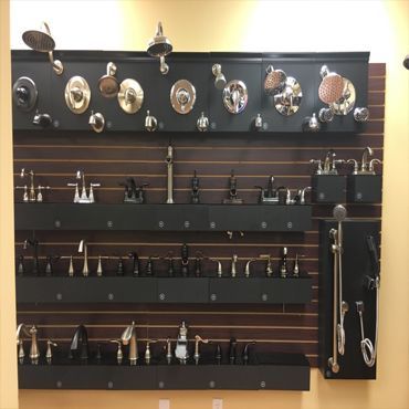 Bathroom fixtures displayed on a wall. Faucets and showerheads in various finishes, arranged on black shelves.