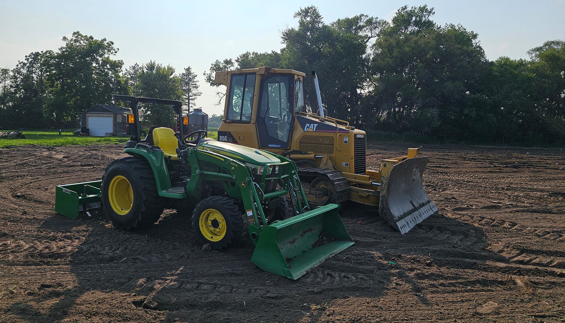 Green tractor and yellow bulldozer parked on a dirt construction site under bright sunlight