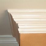 Close-up of white crown molding at the top of a wall, with a section of tan wall visible beneath.