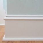 White trim molding on light green wall and wood floor.