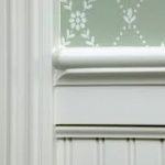 White wainscoting and molding meet a light green patterned wallpaper, suggesting a home interior.