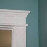White ornate molding frames a window or door against a teal-colored wall.