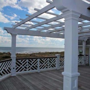 A white pergola over a wooden deck overlooking the ocean.