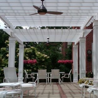 A patio with tables and chairs under a pergola with a ceiling fan
