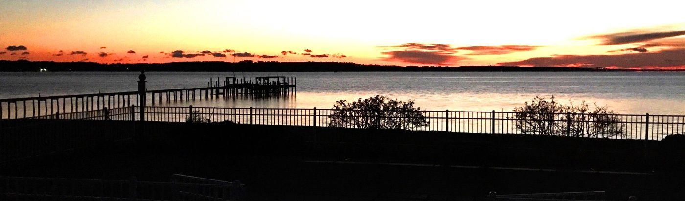 A sunset over a body of water with a fence in the foreground.